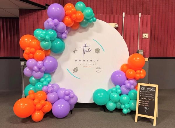 Colorful balloon arch decorating a circular backdrop for a monthly movie project event.