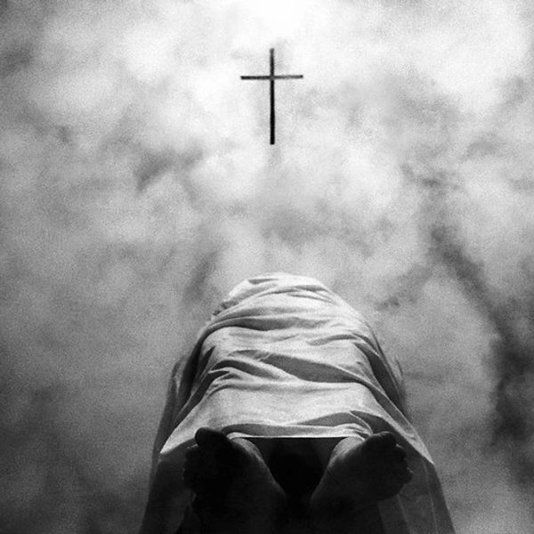 Person kneeling in prayer beneath a cross in a misty atmosphere.