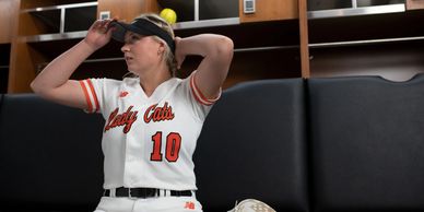 Woman softball player adjusting cap in locker room.