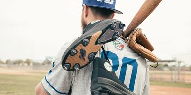 Baseball player holding bat and cleats over shoulder.