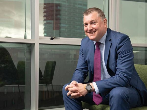 Man in a suit sitting on a chair, smiling.
