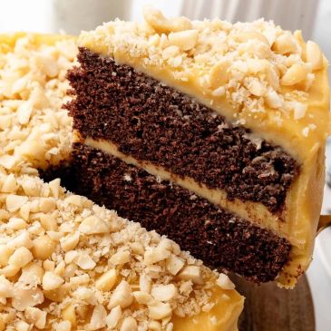 Chocolate cake with yellow frosting and chopped nuts.
