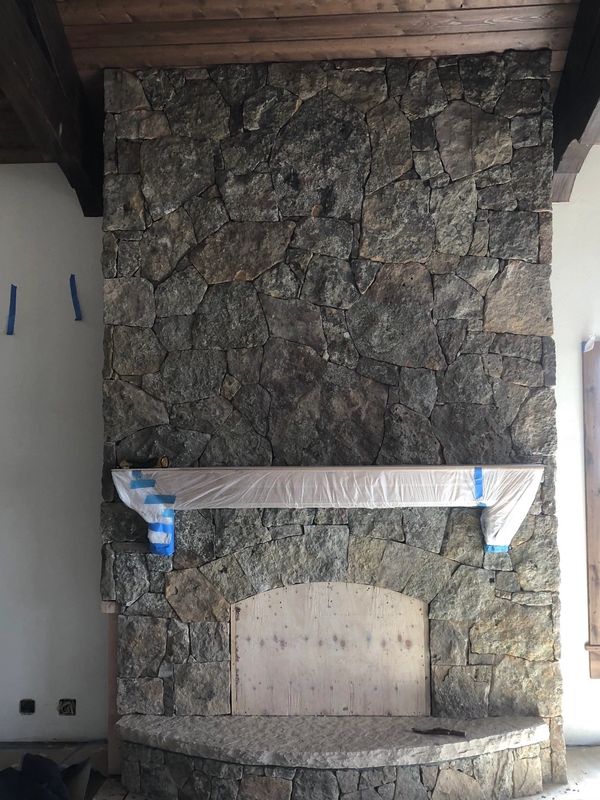 Stone fireplace under construction, with a protective wrap on the mantel.