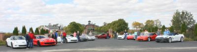 A lineup of colorful sports cars parked outdoors with people mingling around.