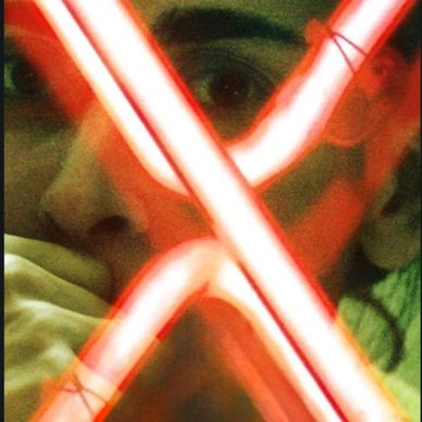 Person's face illuminated by red neon lights forming an X shape.