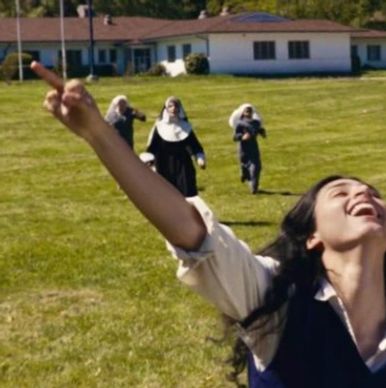 A joyful woman running with nuns chasing her across a grassy field.