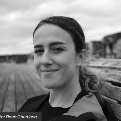 Young woman smiling softly sitting on a wooden bench outdoors.