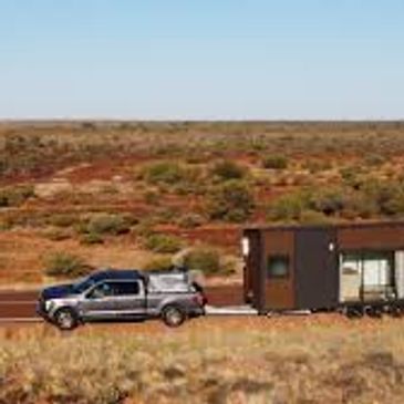 A pickup truck towing a tiny house in a desert landscape.