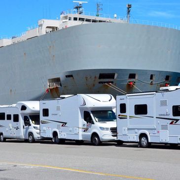 A line of white RVs parked near a large docked ship.