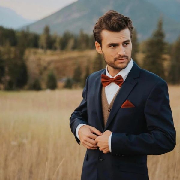 Man in a navy suit with a red bow tie standing in a field.