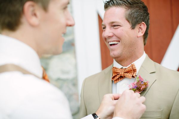 Two men smiling, one adjusting the other's boutonniere.