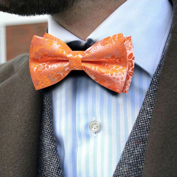 A man wears a vibrant orange floral bow tie with a suit and light blue striped shirt.