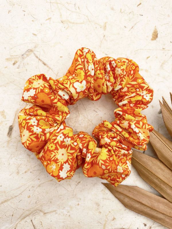 A vibrant orange floral fabric scrunchie on a textured surface.