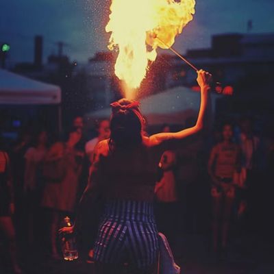 A fire performer breathes a large flame at night in front of an audience.