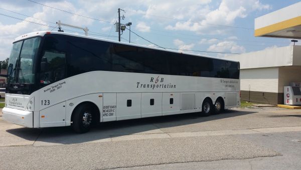 A white R&amp;B Transportation bus parked outside under a partly cloudy sky.