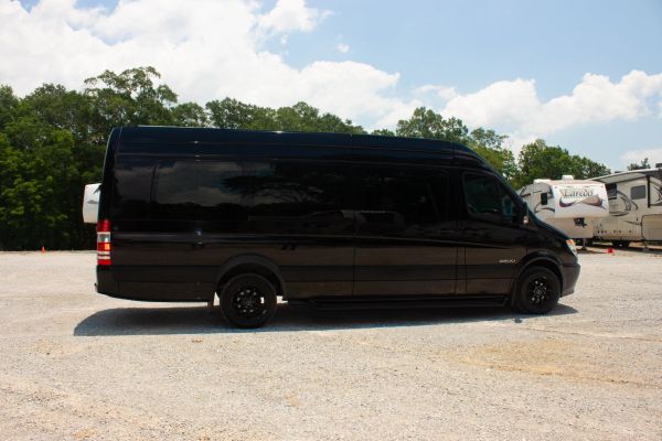 Black cargo van parked on gravel under blue sky.