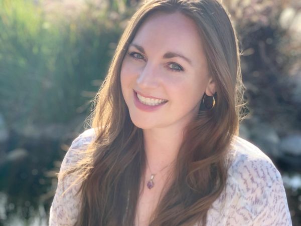 Smiling woman with long brown hair outdoors in soft sunlight.