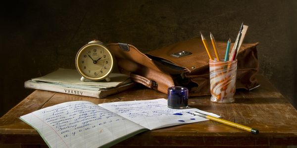 A vintage study setup with an alarm clock, notebooks, pencils, and ink on a wooden table.