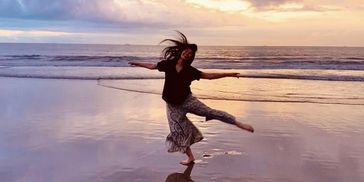 Woman dancing with joy on the beach at sunset.