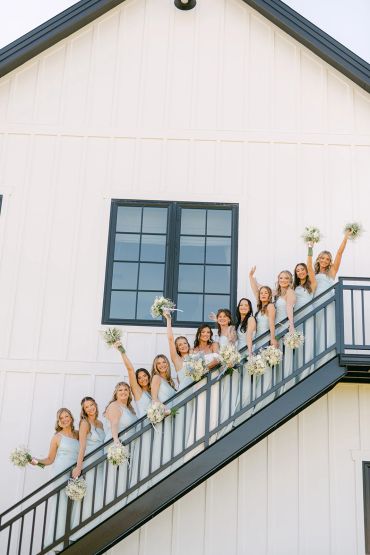 Bridesmaids in matching dresses posing on outdoor staircase with bouquets.