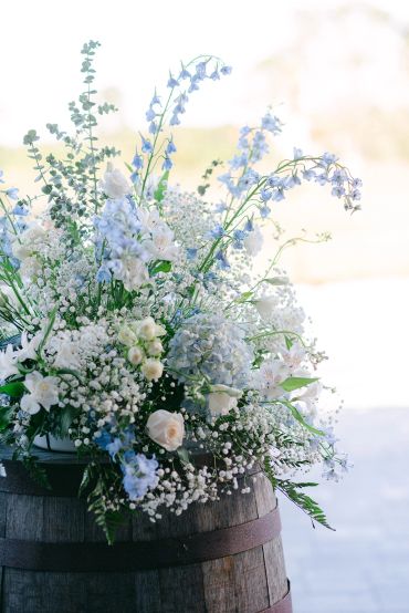 Elegant floral arrangement with white and blue flowers on a wooden barrel.