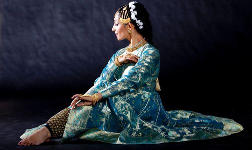 A woman in traditional attire poses gracefully against a dark backdrop.