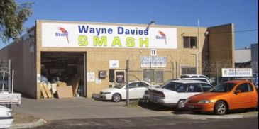 Auto repair shop named Wayne Davies Smash with parked cars outside.