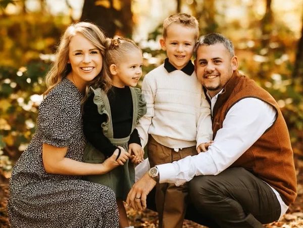 A happy family poses together in a sunlit autumn forest.