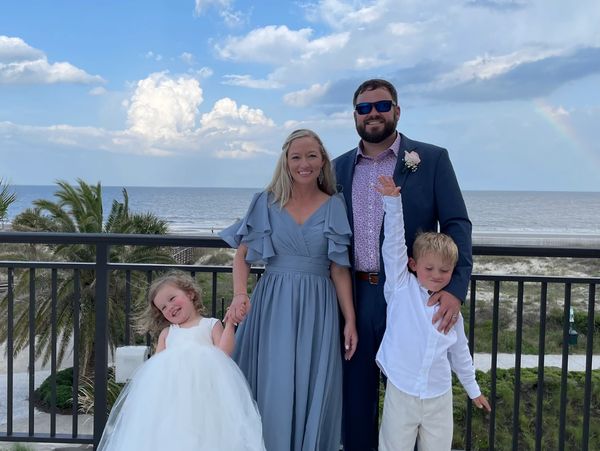 A family dressed formally posing outdoors near the beach with a rainbow in the background.