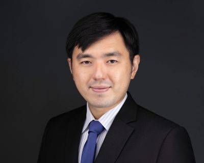 Professional headshot of a man in a suit and blue tie against a dark background.