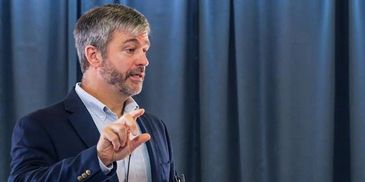 Man in a suit explaining something with a hand gesture.