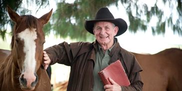 Smiling elderly man in cowboy hat with horse and book.