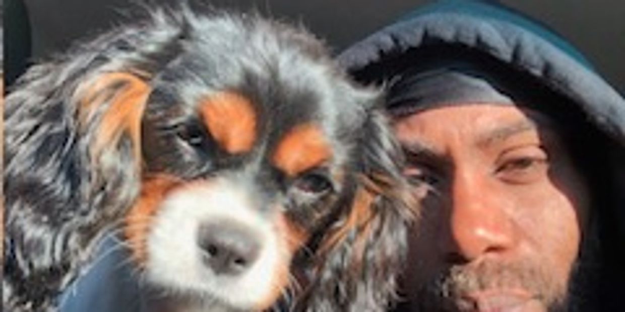 Man in hoodie with a small dog in sunlight.