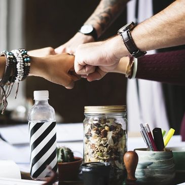 Four people fist bump over a table with snacks and stationery.