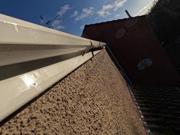Close-up of a house exterior wall and gutter under a blue sky.