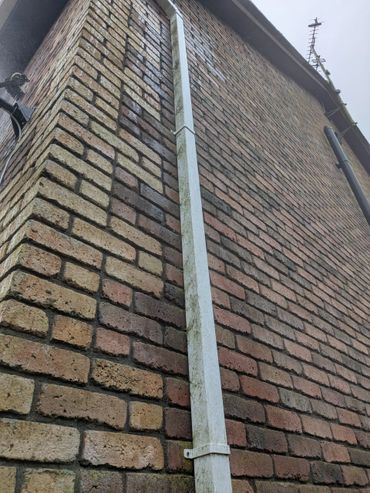 White drainpipe attached to a brick wall under a cloudy sky.