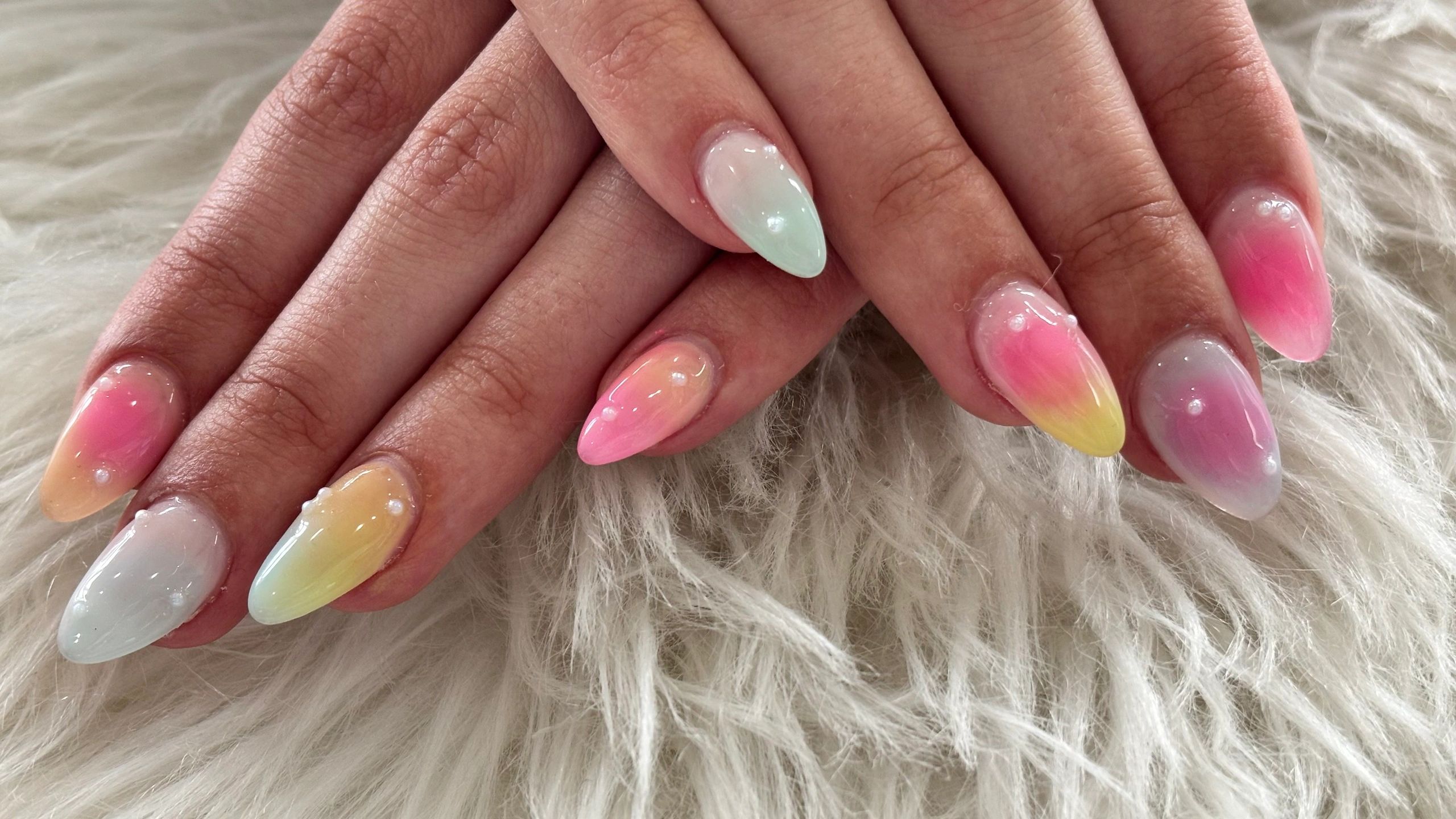 Gradient pastel-colored almond nails with glossy finish and pearl accents.