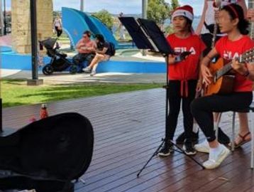 Children singing and playing guitar outdoors in festive attire.