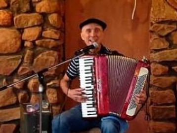 Smiling man playing a red accordion indoors with a stone wall background.