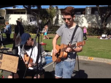 Two young musicians performing outdoors on a sunny day.