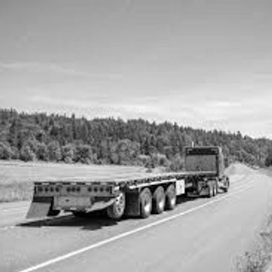A flatbed truck driving on a highway under a clear blue sky.