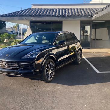 Sleek black Porsche SUV parked in a lot near a building with tiled roof.