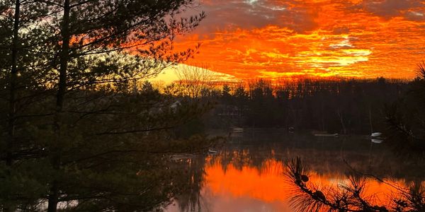 Sunset over a lake with vibrant orange sky and silhouetted trees.