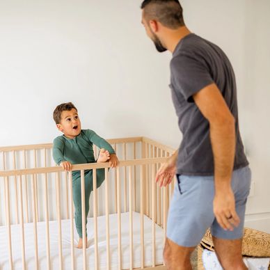 A toddler trying to climb out of his crib, dad trying to stop him 