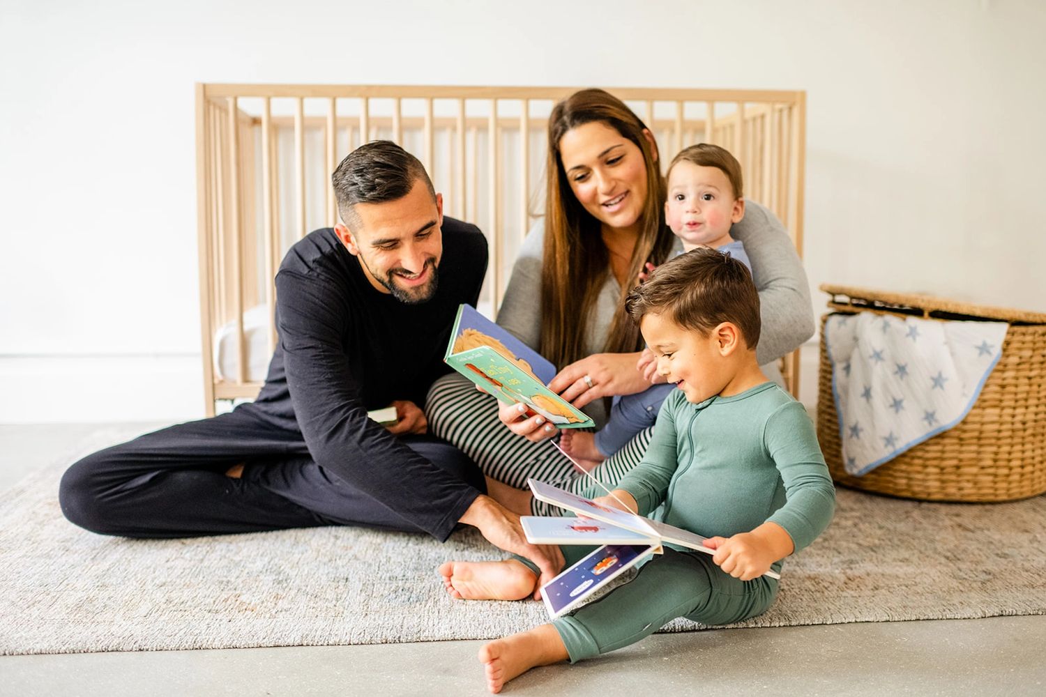 Family of four reading books together for bedtime routine. Mom, dad, baby, toddler