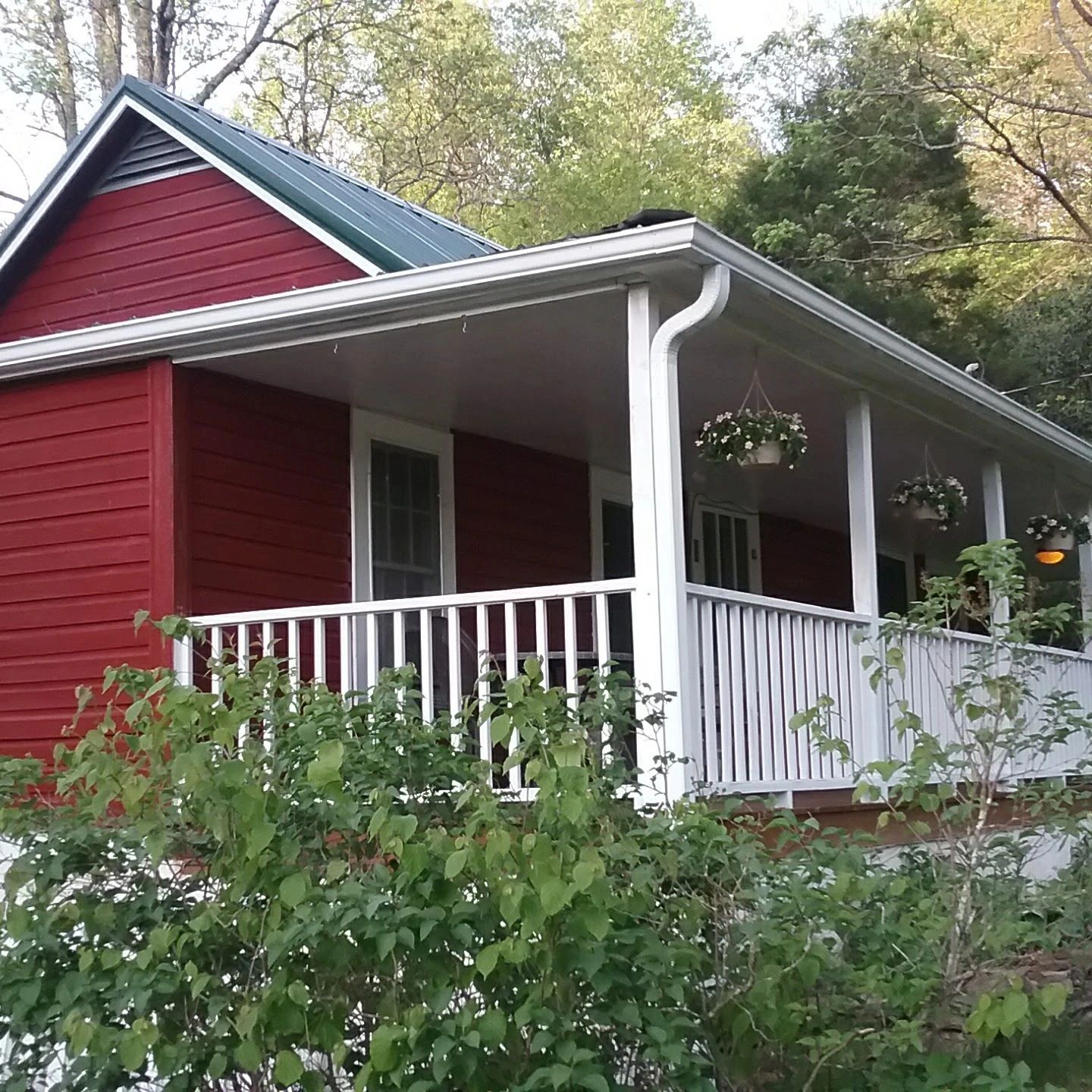 Red house with white porch railing and hanging flower pots.