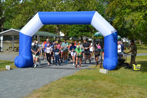 Runners start a race under a blue and white inflatable arch on a park path.