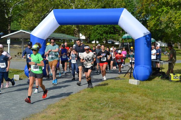Runners starting a race under a blue and white inflatable arch in a park.