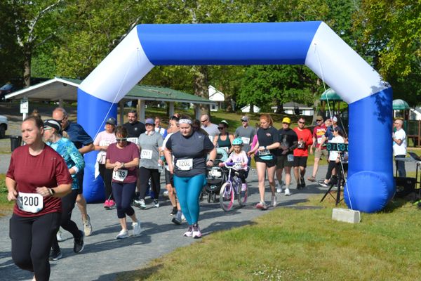 Runners starting a race under a blue and white inflatable arch on a sunny day.