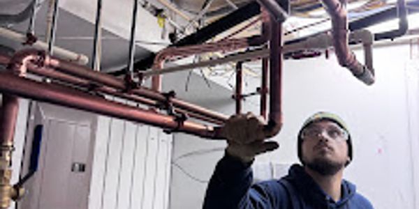 Worker inspecting copper piping in an industrial setting.